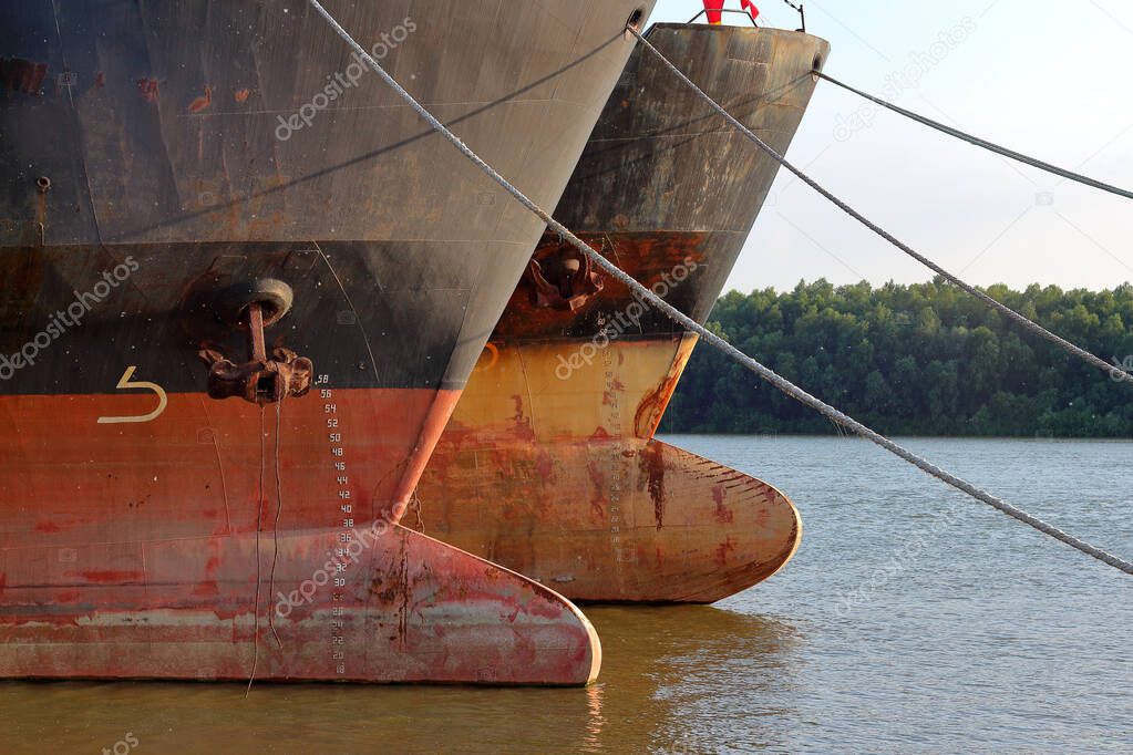 Prows of two old rusty ships with anchor chain anchored at Danube river at summer