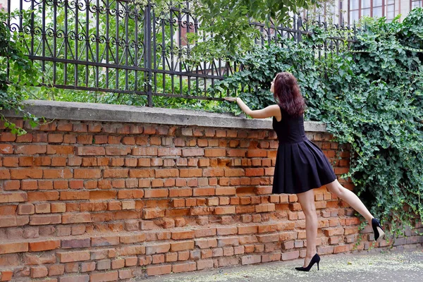 Beautiful Girl Black Dress Peeks Brick Fence Forged Fence Covered — Stock Photo, Image