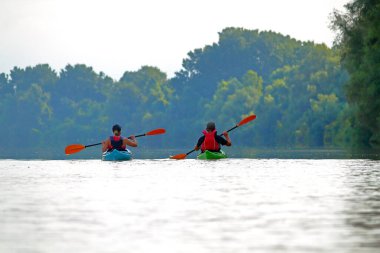Yazın Tuna Nehri 'nde kayak yapan genç ve güzel bir çiftin arka planda yeşil ağaçlarla görüntüsü. Su üzerindeki turizm ve açık hava aktiviteleri kavramı