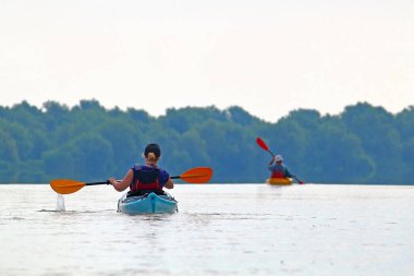 İki kano içindeki insanların dikiz aynasından. Yazın Tuna Nehri 'nde kayak yaparken arka planda yeşil ağaçlar vardı. Sudaki turizm ve açık hava aktiviteleri kavramı