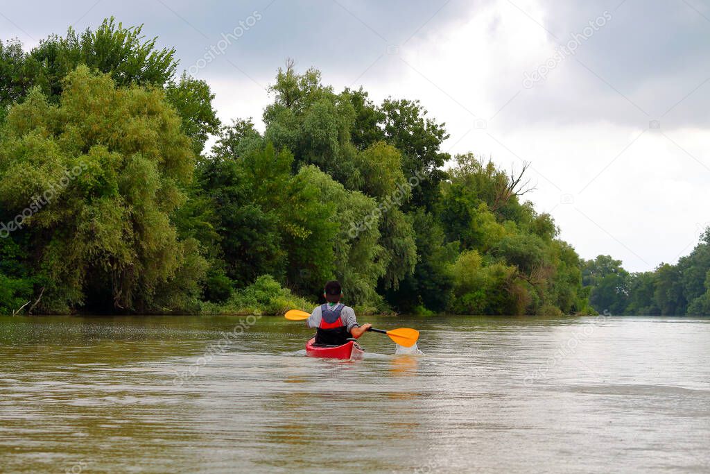 Rear view of teenager paddle red kayak on summer Danube river. Summer kayaking. Concept for adventure, travel, action, lifestyle