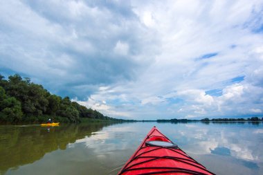 Sakin bir yaz gününde Tuna Nehri 'nde kano yaparken. Nehirde ve mavi gökyüzünde kırmızı kano pruvasına bakın. Su turizmi ve macera