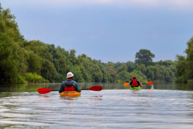 İki kano içindeki insanların dikiz aynasından. Yazın Tuna Nehri 'nde kayak yaparken arka planda yeşil ağaçlar vardı. Sudaki turizm ve açık hava aktiviteleri kavramı