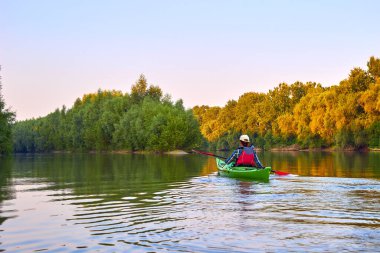 Woman paddle green kayak. Kayaking near overgrown shore of green thick thickets, wild grapes and driftwood on the banks of river at summer. Concept for adventure, travel, action, lifestyle.