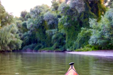 Tuna Nehri 'nde kırmızı kano yayı. Yaz kayığı, aşırı büyümüş yeşil ağaçların ve vahşi üzümlerin kıyılarında.