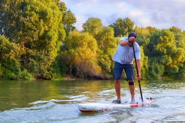 Man on stand up paddle boarding on Danube river at summer morning.