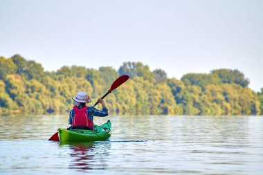 Zarif hasır şapkalı kanocu kadın Tuna Nehri 'nde yeşil kano sürüyor. Yaz Suyu Sporu