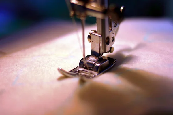 Kumaş ve iplikle dikiş makinesi. Donanım lambasının ışığıyla çalışıyor. Çelik iğne, balgam ve presör ayaklı yakın çekim..