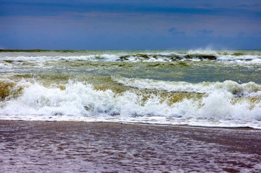 View of storm seascape with sandy beach at cloudy day. Waves in the sea and sand on the beach against stormy sky