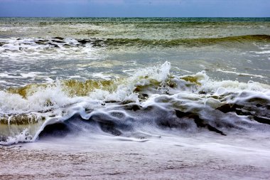 View of storm seascape with sandy beach at cloudy day. Waves in the sea and sand on the beach against stormy sky