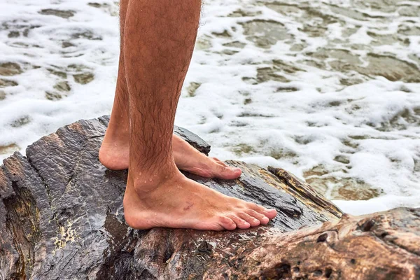 Legs of a man standing on a snag on the seashore