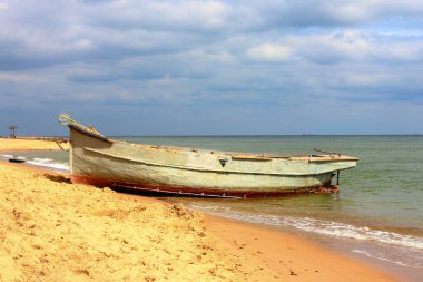 Fishing boat on the sandy sea beach and cloudy sky