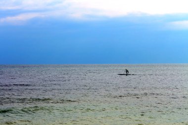 Silhouette of active surfer on stand up paddle board paddling in sea