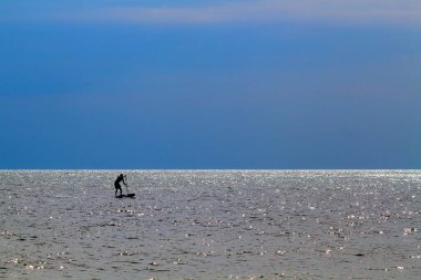 Silhouette of active surfer on stand up paddle board paddling in sea