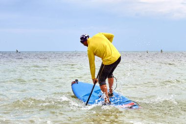 Athletic man paddling on stand up paddle board (paddleboard, SUP) on sea. Stand up paddle boarding - awesome active recreation in nature. Back view.