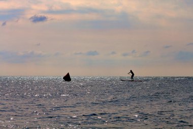 Silhouette of active surfer on stand up paddle board paddling in sea