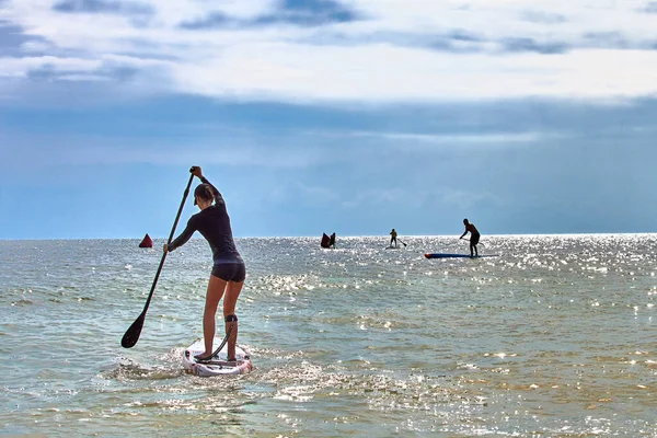 Attractive young girl on stand up paddle boarding SUP rowing on quiet sea. Sport training