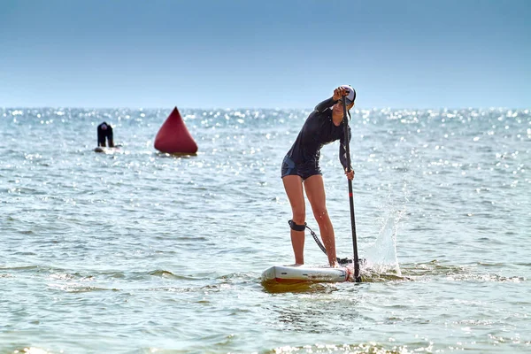 Attractive young girl on stand up paddle boarding SUP rowing on quiet sea. Sport training