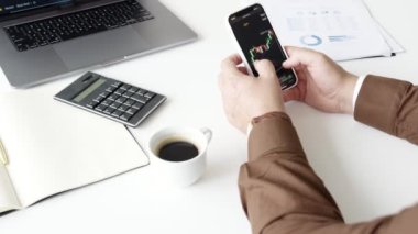 Borsa telefonda. Kahve, dizüstü bilgisayar ve hesap makinesi masada.