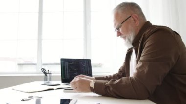 Yaşlı bir adam masadaki bir ofiste çalışır. Borsada ticaret yapıyor.