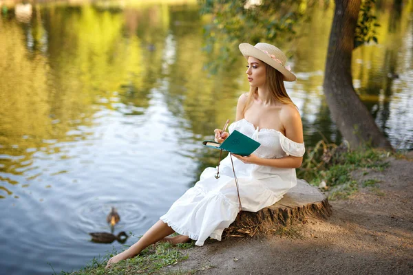 Beyaz elbiseli güzel bayan doğayla ilgili bazı notlar alıyor.