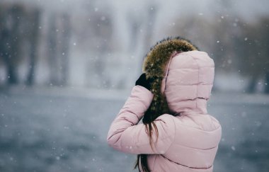 Kapüşonlu genç bir kızın yakından görünüşü denizdeki bir adaya bakıyor.