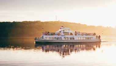 Yürüyen bir gemi turistlerle birlikte gün batımında denizde yüzer.