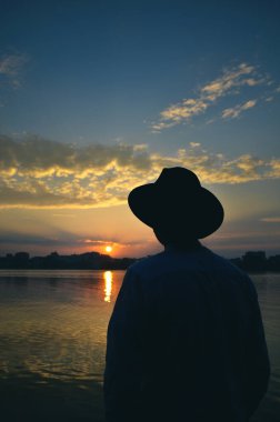 Şapkalı adamın silueti gün batımına bakıyor.
