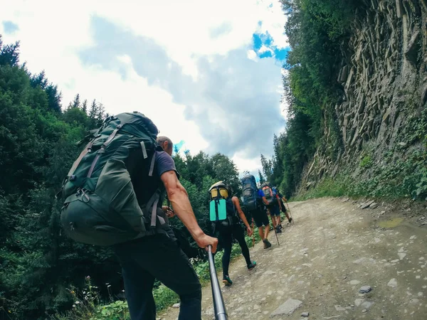 Tourists with backpacks climb the mountain road