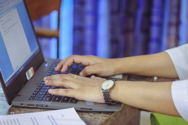 Typing on a laptop keyboard in a office room by a business person