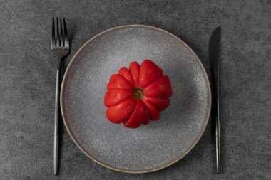 Gri bir tabakta kırmızı domates. Koyu renkli minimalist masa ayarı. Sağlıklı gıda konsepti. Dünya Vejetaryen Günü.
