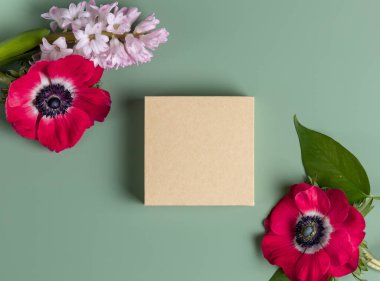 Beige cardboard box surrounded by flowers on green background.