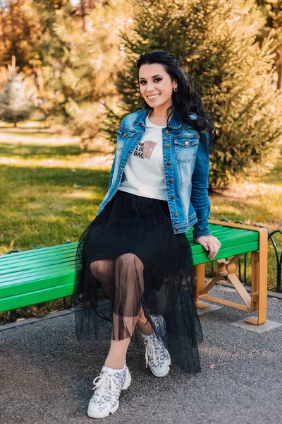 The brunette is beautiful, with beautiful makeup, posing on a bench in an autumn park — Stock Photo, Image