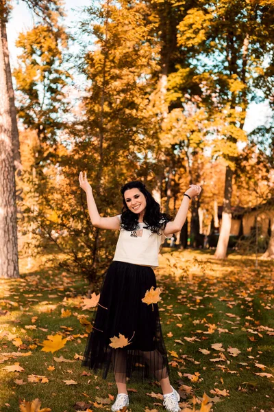 La morena es hermosa, con hermoso maquillaje, lanzando hojas en el parque de otoño —  Fotos de Stock