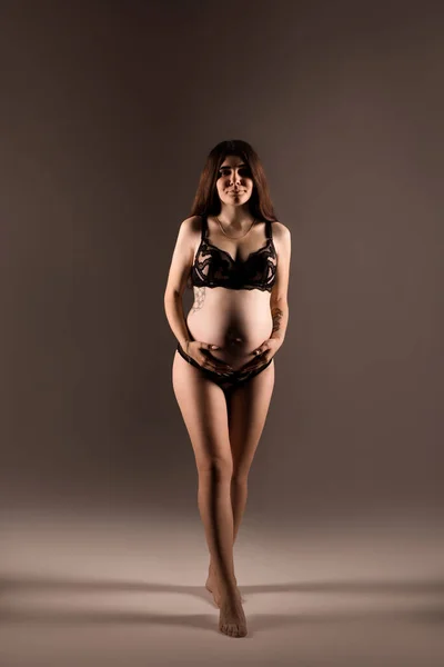 Donna incinta in lingerie abbraccia il ventre con le mani — Foto Stock