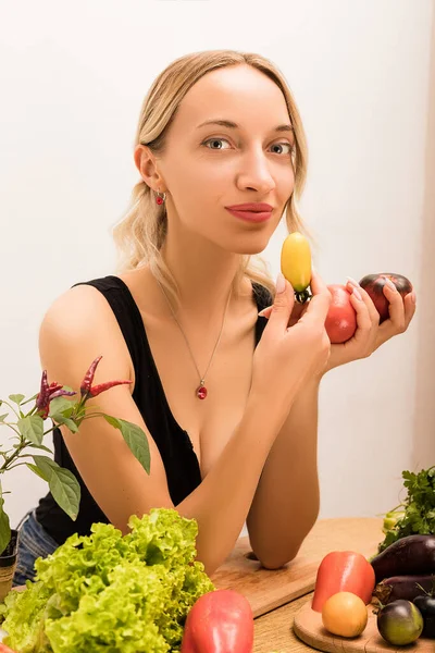 Giovane bella donna che tiene i pomodori tra le mani mentre è seduta a tavola in cucina — Foto Stock