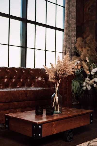 Vaso con fiori secchi si erge su un tavolo di legno all'interno — Foto Stock