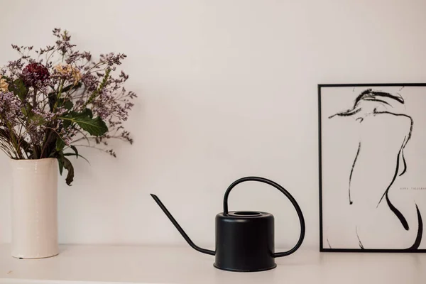 Un irrigatore di fiori neri si trova su uno scaffale bianco vicino a fiori e dipinti — Foto Stock