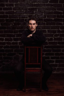 Genç yakışıklı bir adam sandalyeye oturur ve elini sandalyenin arkasına yaslar..