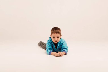 Mavi ceketli küçük bir çocuk beyaz arka planda yatıyor.