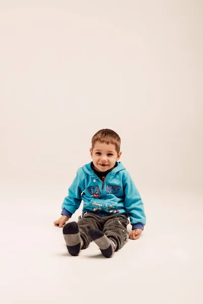 Mavi ceketli küçük bir çocuk beyaz arka planda oturuyor. — Stok fotoğraf