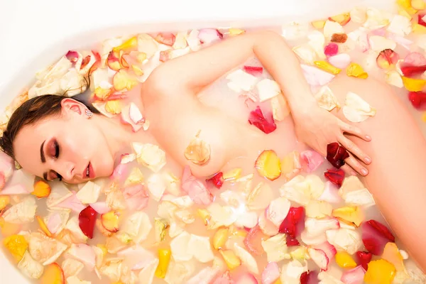 Hermosa joven cerrando los ojos toma un baño con pétalos de rosa — Foto de Stock