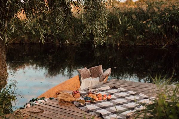 Ekose bir battaniyenin üzerinde su kıyısındaki iskelede meyve ve tatlı var.