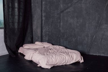 Beyaz yataklı yatak pencerenin yanındaki karanlık bir odada duruyor.