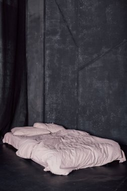 Beyaz yataklı yatak pencerenin yanındaki karanlık bir odada duruyor.