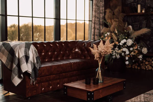 Un vaso con fiori secchi poggia su un tavolo di legno accanto al divano e alla finestra. — Foto Stock