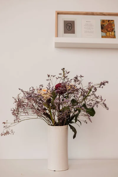 A white vase with wildflowers stands on a white shelf in the interior — ストック写真