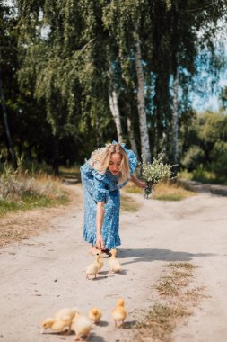 Kırsal kesimden genç bir kadın küçük ördekleri beslemek için eğildi.