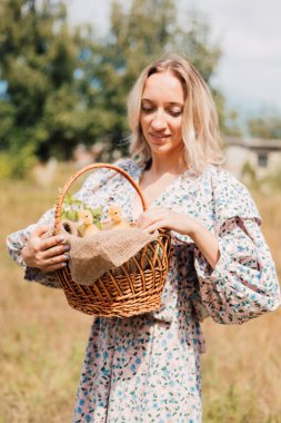 Genç bir kadın bir sepet ördek yavrusu tutuyor ve gülümsüyor.