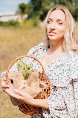 Genç bir kadın bir sepet ördek yavrusu tutuyor ve gülümsüyor.